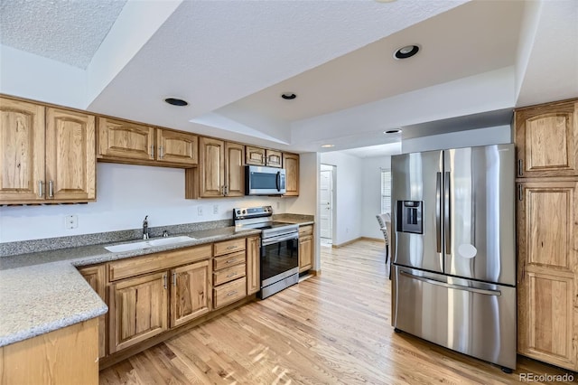 kitchen with a tray ceiling, stainless steel appliances, light wood-type flooring, a sink, and recessed lighting