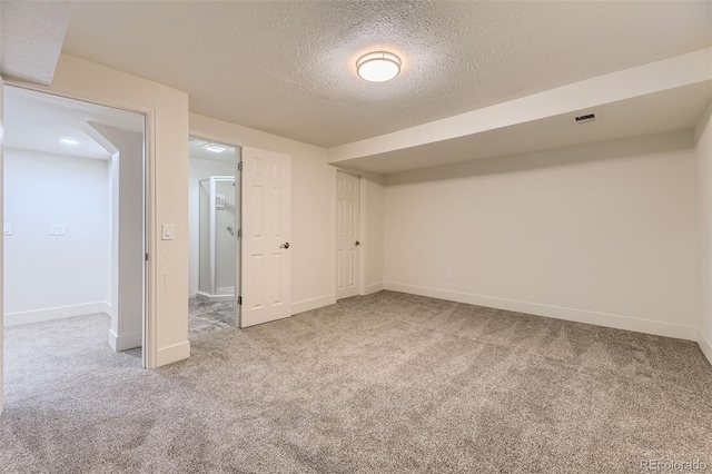 below grade area featuring carpet, visible vents, a textured ceiling, and baseboards