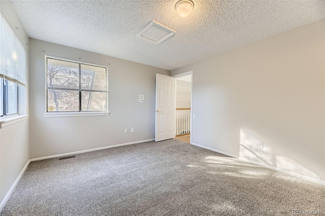 unfurnished room with carpet, a textured ceiling, visible vents, and baseboards