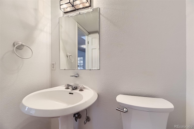 bathroom featuring toilet, a sink, and a textured wall