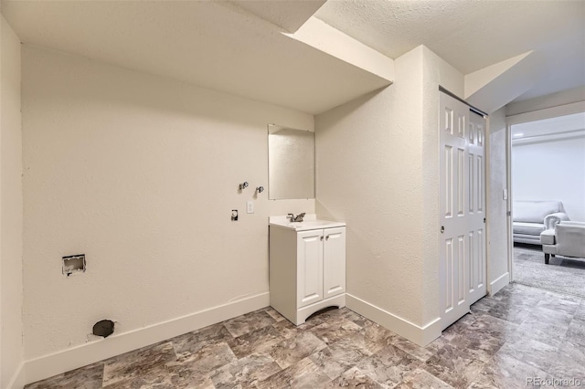 laundry room with a textured wall, laundry area, a sink, and baseboards