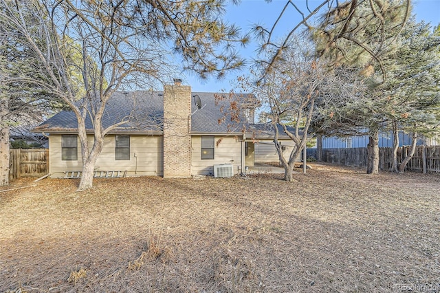 back of property with central AC, a chimney, a fenced backyard, and roof with shingles