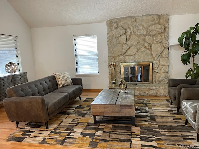 living room featuring a textured ceiling, vaulted ceiling, a fireplace, and wood finished floors