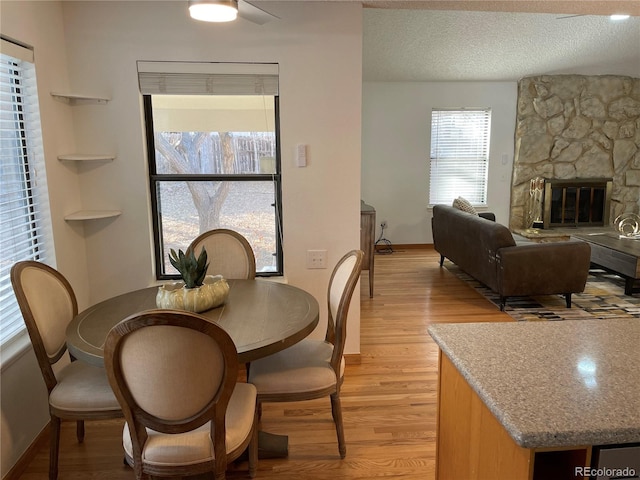 dining space featuring a textured ceiling, a stone fireplace, light wood-style flooring, and baseboards