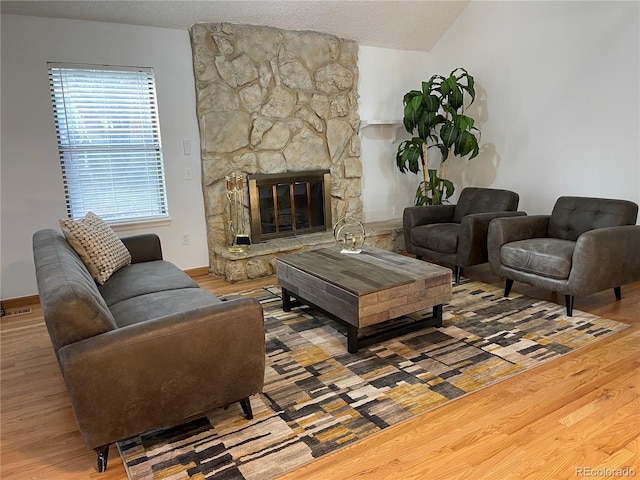 living area featuring a textured ceiling, wood finished floors, and a stone fireplace