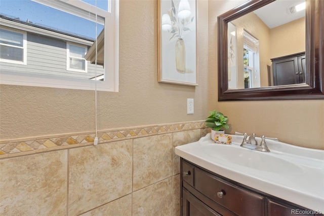 bathroom with a textured wall, wainscoting, vanity, and tile walls