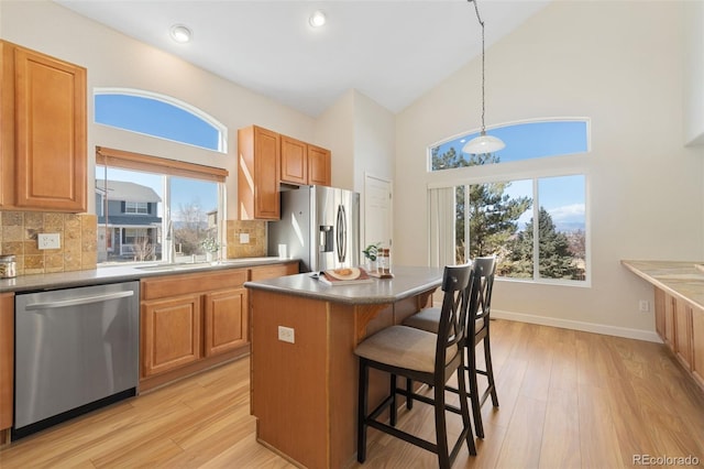 kitchen featuring a kitchen island, hanging light fixtures, appliances with stainless steel finishes, light wood-type flooring, and dark countertops