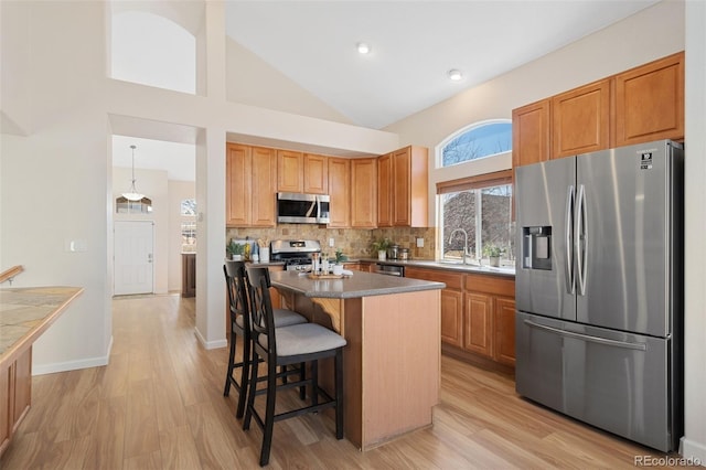 kitchen featuring light wood-style floors, a kitchen island, appliances with stainless steel finishes, and backsplash