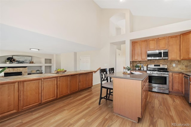 kitchen featuring stainless steel appliances, dark countertops, light wood-style flooring, a kitchen island, and a kitchen bar