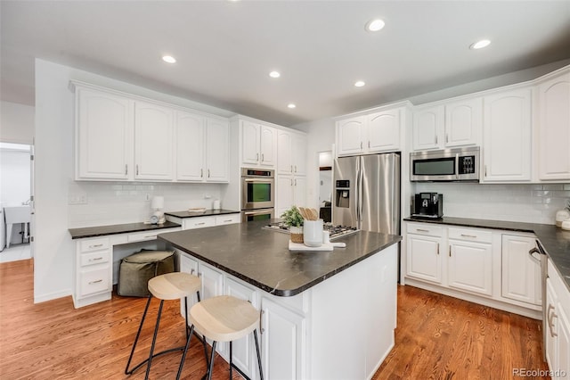 kitchen featuring a kitchen island, white cabinetry, a breakfast bar area, stainless steel appliances, and light wood-type flooring