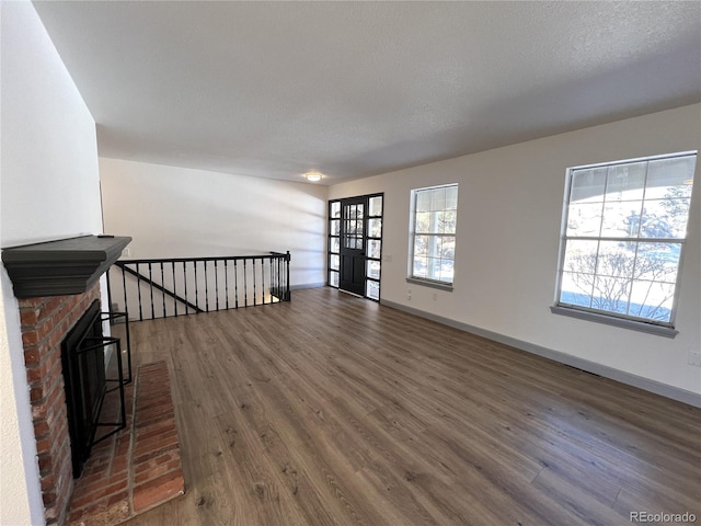 unfurnished living room with dark hardwood / wood-style flooring, a brick fireplace, and a textured ceiling