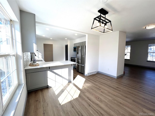 kitchen featuring dark hardwood / wood-style flooring, gray cabinets, stainless steel fridge with ice dispenser, and kitchen peninsula