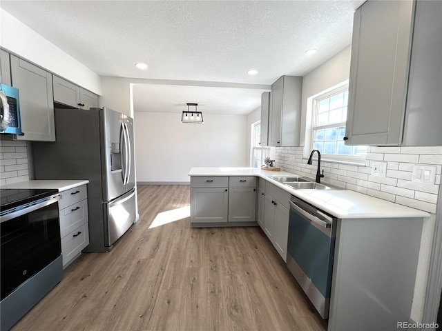 kitchen featuring sink, light hardwood / wood-style flooring, gray cabinets, stainless steel appliances, and decorative backsplash