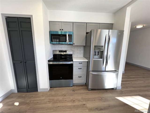 kitchen featuring a textured ceiling, light hardwood / wood-style flooring, appliances with stainless steel finishes, gray cabinets, and backsplash