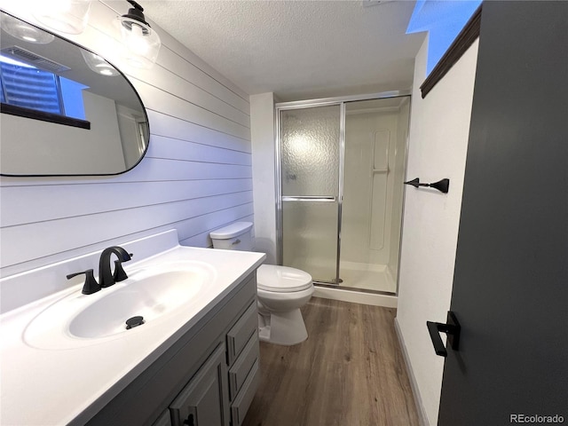 bathroom featuring a shower with shower door, wood walls, hardwood / wood-style flooring, vanity, and a textured ceiling