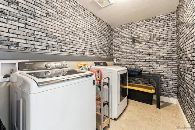 laundry area featuring brick wall, washer / dryer, a textured ceiling, and light tile patterned floors