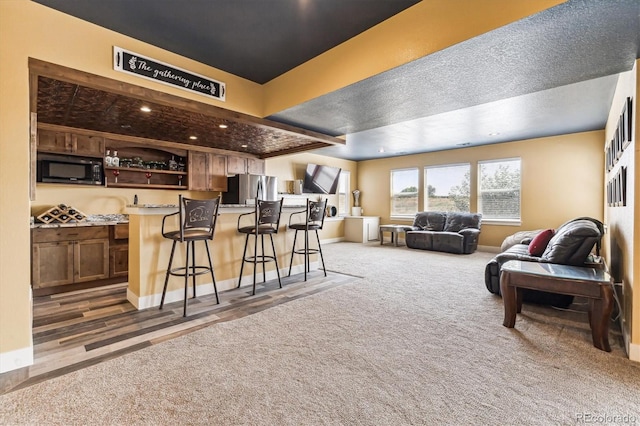 interior space featuring black microwave, stainless steel fridge, carpet flooring, a kitchen breakfast bar, and a kitchen island