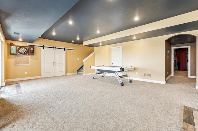 playroom featuring light colored carpet, a barn door, and a textured ceiling