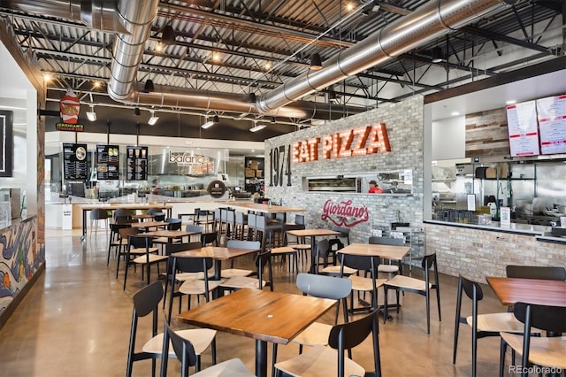 dining room with a towering ceiling, brick wall, and concrete floors