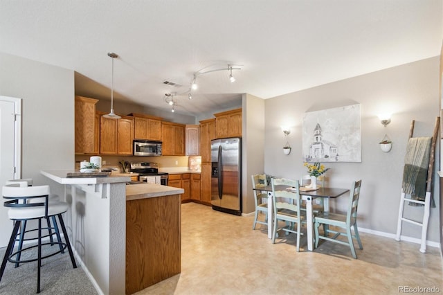 10818 Cimarron St Unit 1102, Firestone, CO 80504 - kitchen with stainless steel appliances, a peninsula, a breakfast bar, brown cabinetry, and decorative light fixtures