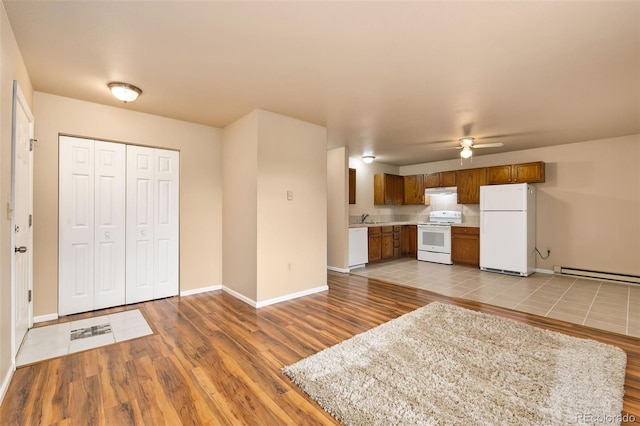 kitchen with baseboard heating, brown cabinetry, white appliances, light wood-type flooring, and baseboards