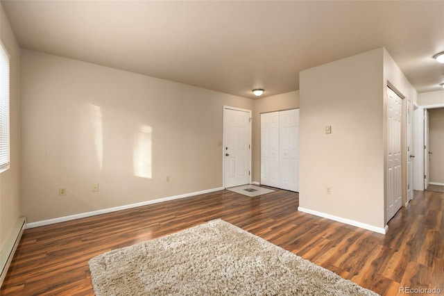 empty room with a baseboard heating unit, baseboards, and dark wood-type flooring