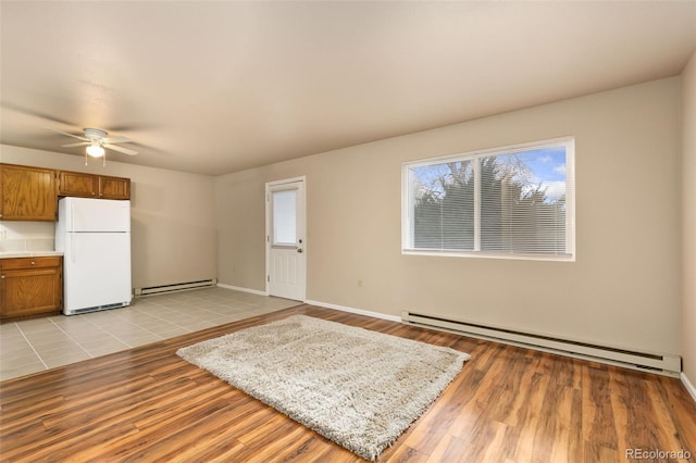 unfurnished living room featuring baseboard heating, a ceiling fan, and a healthy amount of sunlight