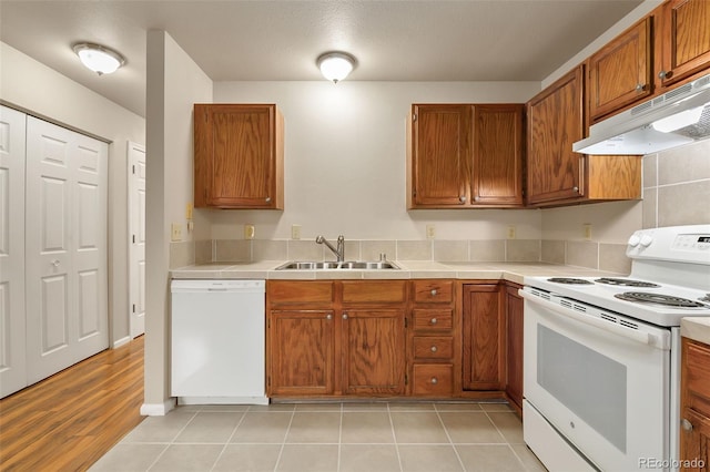 kitchen with under cabinet range hood, white appliances, a sink, and brown cabinetry