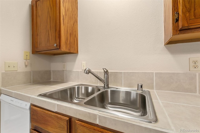 kitchen with dishwasher, brown cabinetry, a sink, and light countertops