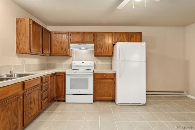 kitchen featuring a baseboard heating unit, brown cabinets, under cabinet range hood, and white appliances