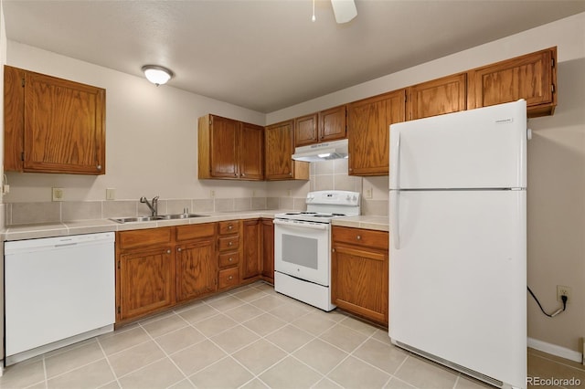 kitchen with brown cabinets, under cabinet range hood, a sink, light tile patterned floors, and white appliances