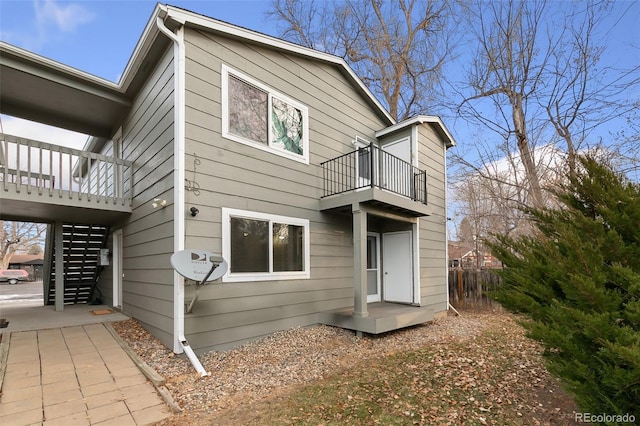 rear view of property with fence, a balcony, and stairs