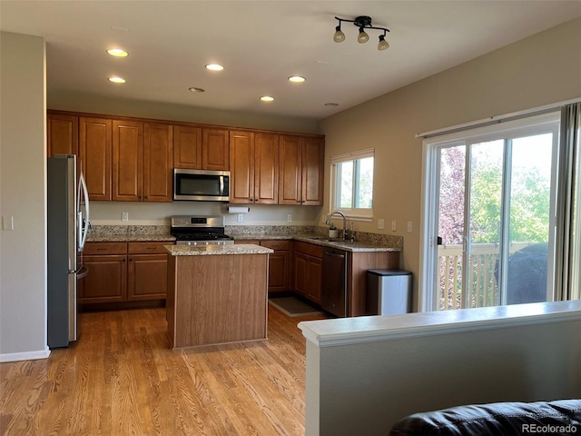 kitchen featuring light wood-type flooring, light stone counters, a center island, sink, and appliances with stainless steel finishes