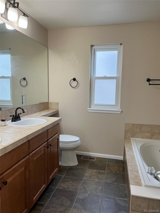 bathroom featuring vanity, tiled tub, and toilet