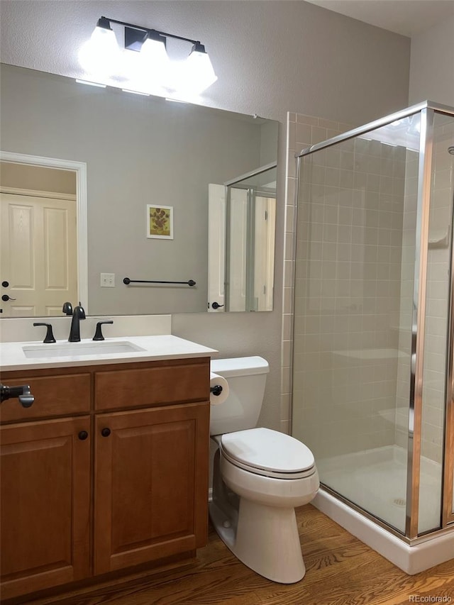 bathroom with hardwood / wood-style floors, a shower with shower door, vanity, and toilet