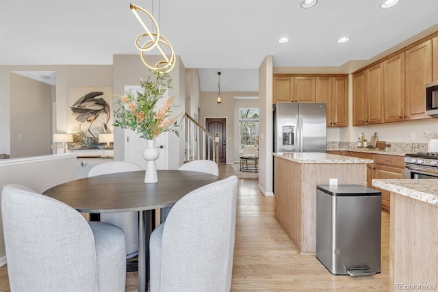 kitchen featuring light stone counters, decorative light fixtures, a center island, appliances with stainless steel finishes, and light hardwood / wood-style floors