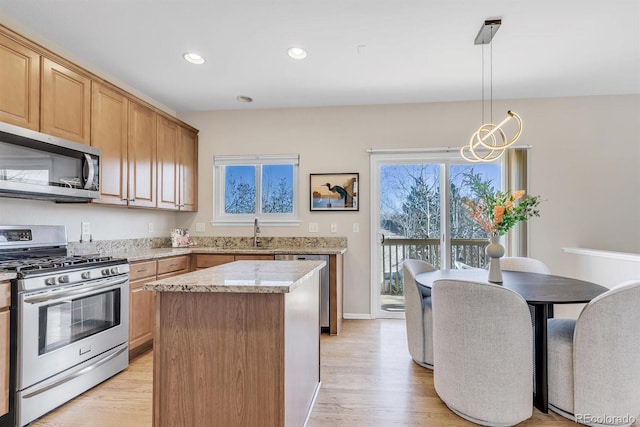 kitchen featuring a kitchen island, pendant lighting, stainless steel appliances, light stone countertops, and light wood-type flooring