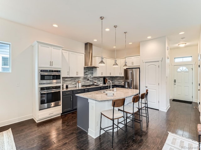 10479 E 25th Dr, Aurora, CO 80010 - kitchen featuring stainless steel appliances, wall chimney exhaust hood, dark wood finished floors, decorative backsplash, and a breakfast bar area