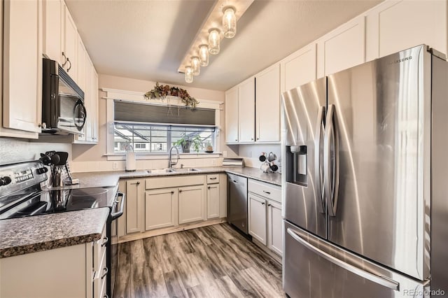 kitchen with stainless steel appliances, wood finished floors, a sink, and white cabinets