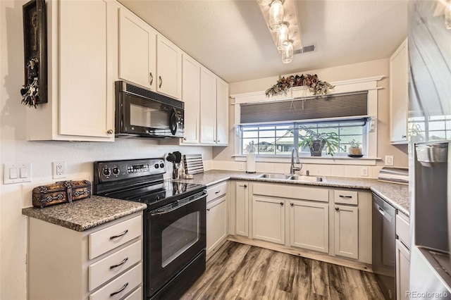 kitchen with white cabinetry, a sink, wood finished floors, dark stone counters, and black appliances