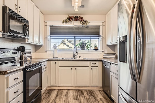 kitchen with white cabinetry, a sink, dark stone countertops, wood finished floors, and black appliances