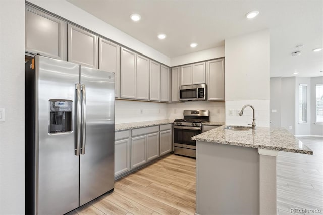 3831 E 141st Ave, Thornton, CO 80602 - kitchen featuring appliances with stainless steel finishes, a sink, gray cabinets, a peninsula, and light wood finished floors