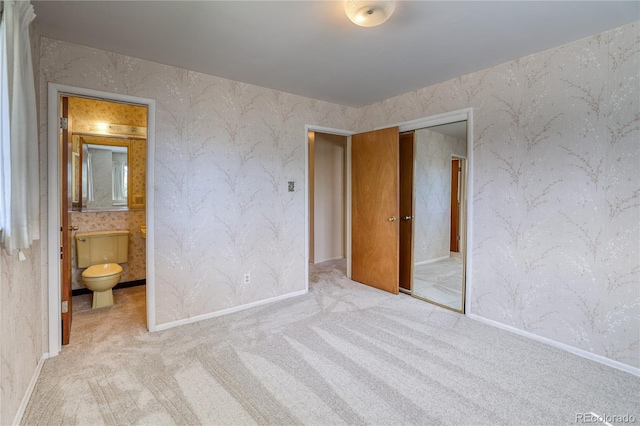 unfurnished bedroom with wallpapered walls, a closet, carpet floors, connected bathroom, and baseboards