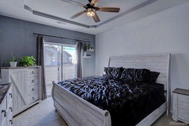 carpeted bedroom featuring access to exterior, ceiling fan, and a tray ceiling