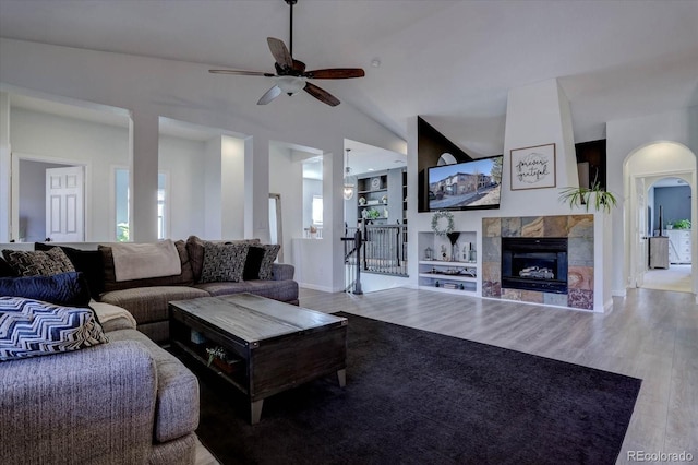 living room featuring built in shelves, high vaulted ceiling, a tile fireplace, ceiling fan, and light hardwood / wood-style floors