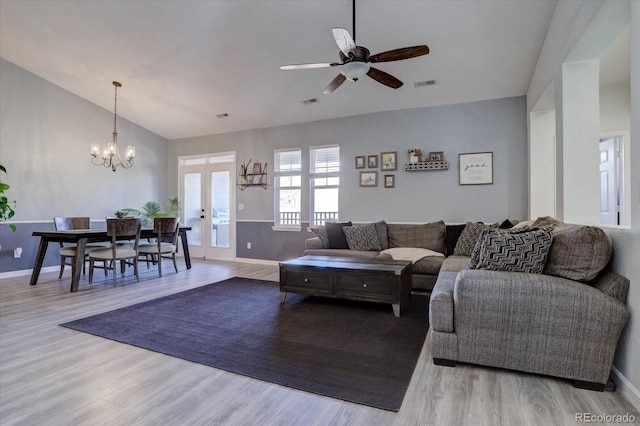 living room with vaulted ceiling, ceiling fan with notable chandelier, light wood-type flooring, and french doors