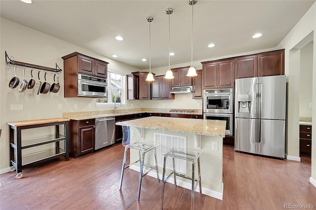 kitchen with hanging light fixtures, dark wood-type flooring, a center island, and stainless steel appliances