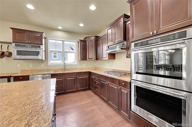 kitchen with sink, appliances with stainless steel finishes, light stone counters, and light hardwood / wood-style floors