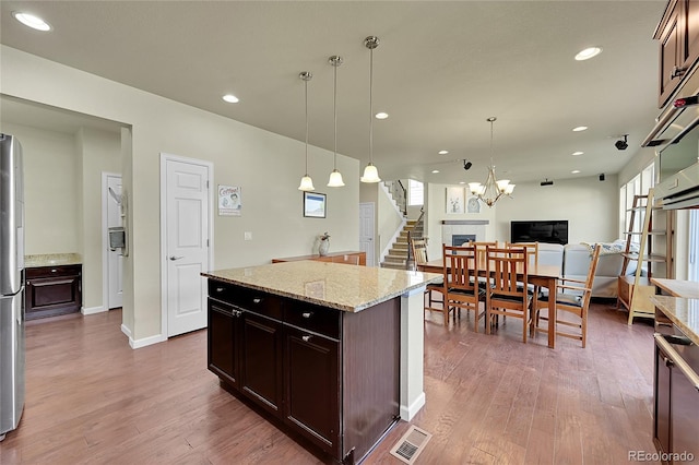 kitchen featuring light stone counters, hanging light fixtures, a kitchen island, a chandelier, and wood-type flooring