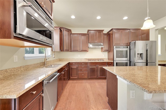 kitchen with light wood-type flooring, a center island, light stone countertops, appliances with stainless steel finishes, and decorative light fixtures